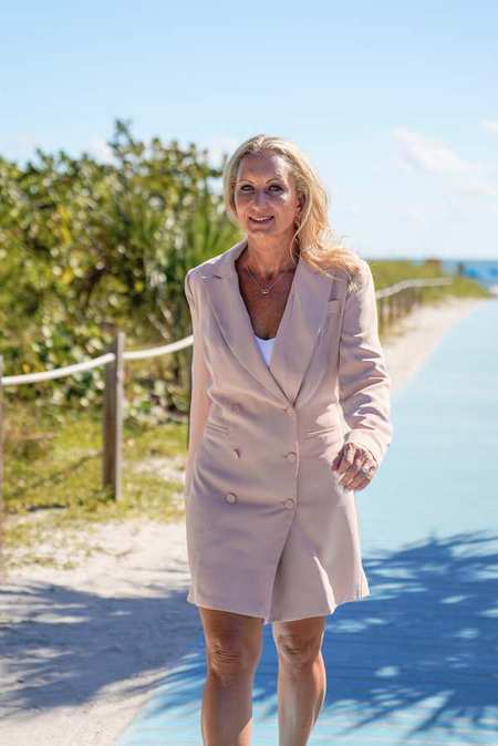 Dr. Lori Kalie walking confidently toward the camera on a beach path